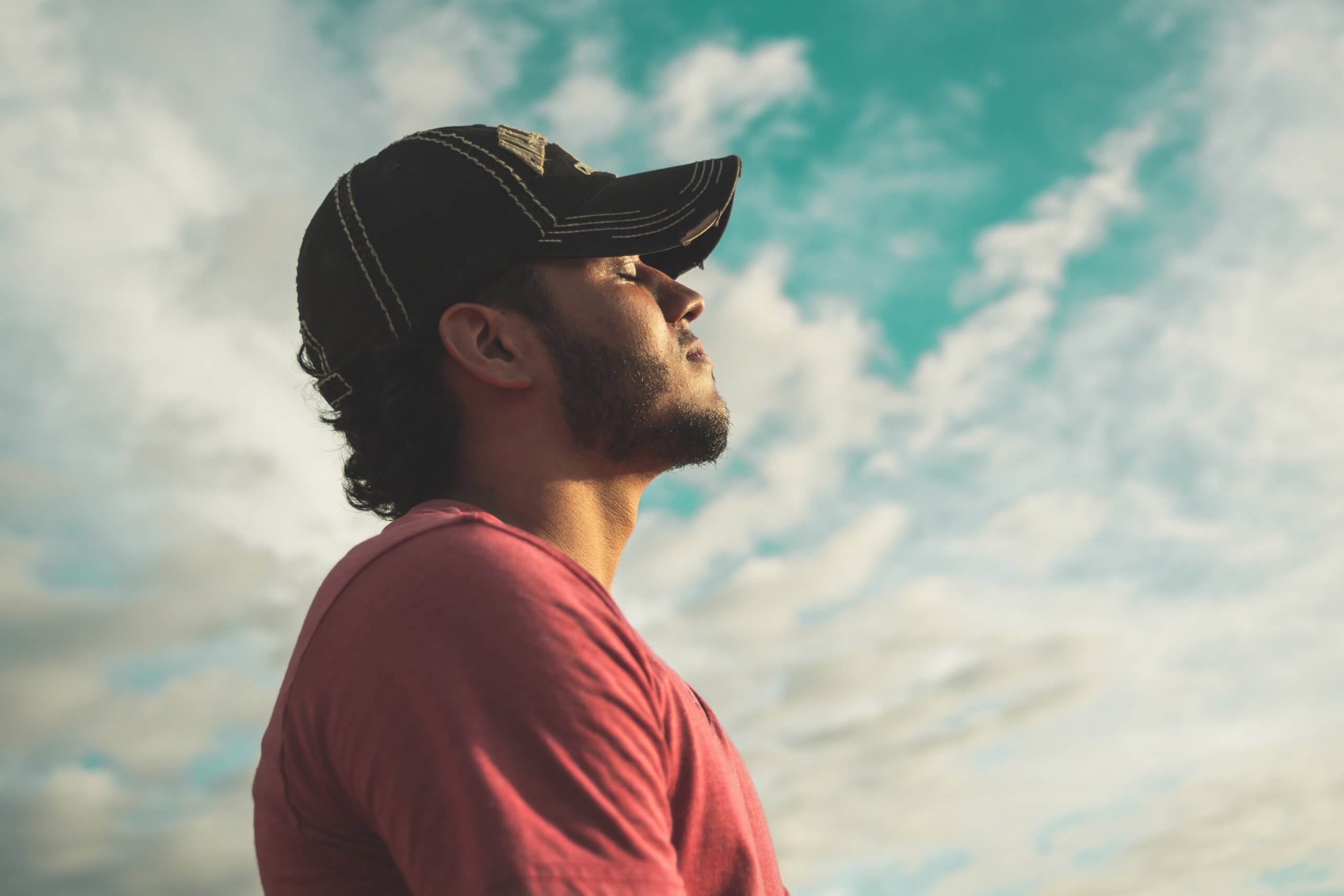 man-wearing-black-cap-with-eyes-closed-under-cloudy-sky-810775